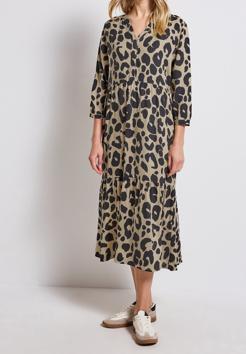 Femme portant une robe imprimé léopard mi-longue à manches longues avec une jupe à étages, associée à des baskets blanches et beige.