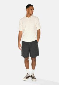 Kurzärmliges cremefarbenes Polohemd mit strukturiertem Muster, kombiniert mit dunkelgrauen Shorts und braunen Sneakers mit weißen Schnürsenkeln sowie Socken.