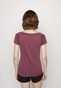 Mörkt vinröd kortärmad topp med rundad halsringning och raglanärmsdesign. Slät textur, figurnära silhuett och enfärgad tyg utan mönster.