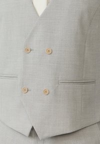 Gilet gris à carreaux avec un avant croisé, doté de boutons beiges et de deux poches latérales, réalisé en tissu texturé.