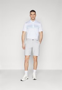 Hvitt polo skjorte med et blått stripemønster, kombinert med lysegrå shorts. Antrekket er komplettert med hvite sneakers og sokker.