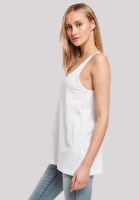 White cotton tank top with a scoop neck, relaxed fit, and wide straps. Worn with light blue denim jeans, showcasing a simple design.