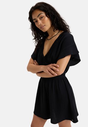 Black dress made of textured fabric. Features a deep V-neck, short sleeves, and an elastic waistband, with a slight flare at the hem.
