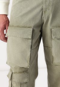 Olivenfarvede cargo-bukser med en glat bomuldsfinish, der har to store klaplommer på lårene og et afslappet fit-design.