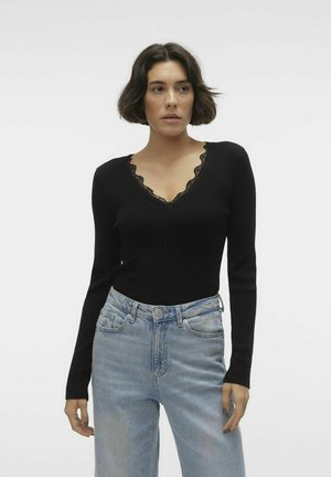 Top negro de manga larga acanalado con escote en V y acabado de encaje, combinado con jeans de tiro alto en azul claro. Textura suave, diseño ajustado.