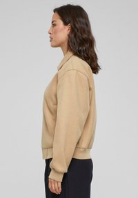 Beige hettegenser med krage, med lange ermer og en avslappet passform. Glatt tekstur, ribbede mansjetter og midjebånd.