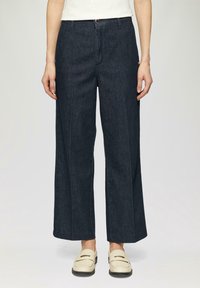 Pantaloni a gamba larga in denim scuro con vita alta, caratterizzati da una piega frontale, chiusura con bottone e ampie tasche laterali.