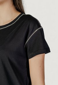 T-shirt nera con maniche corte, scollatura rotonda e cuciture metalliche lungo le spalle per un tocco di dettaglio in più. Tessuto dal tocco morbido.