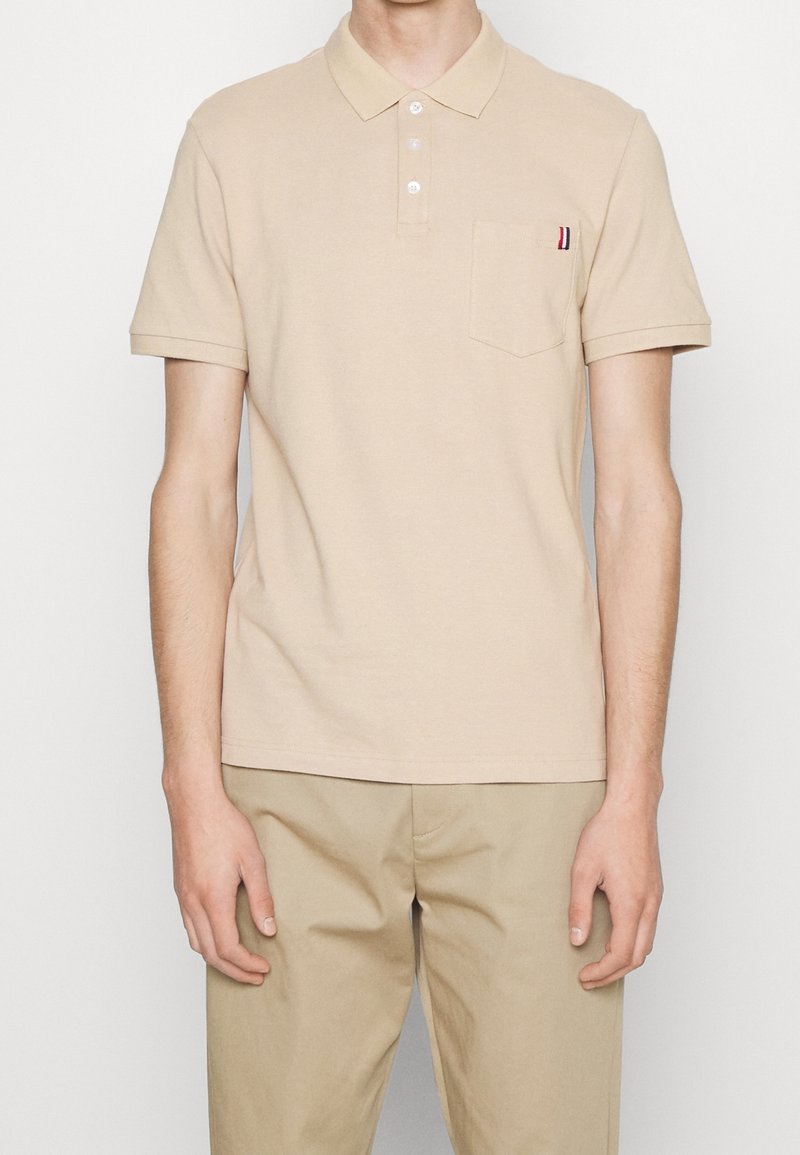 Beige polo tričko vyrobené z bavlny, s knoflíkovou légou, krátkými rukávy a přední kapsou se pruhovaným akcentem.