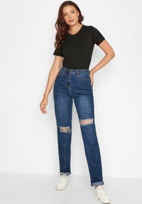 Czarna dopasowana koszulka, dżinsy z wysokim stanem w niebieskim kolorze z przetarciami na kolanach oraz białe sneakersy. Gładki materiał, luźny krój i klasyczny odcień niebieskiego.