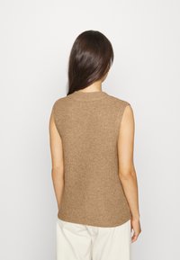 Beige mouwloze trui met een geribbelde textuur, ronde halslijn en een aansluitende pasvorm, gecombineerd met crèmekleurige, loszittende broek.