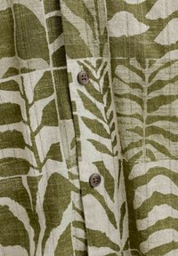 Κοντινό πλάνο υφάσματος με πράσινο και λευκό μοτίβο φύλλων και δύο καφέ κουμπιά ραμμένα σε ένα ένδυμα.