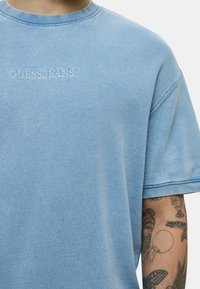 T-shirt oversize blu chiaro con scollatura rotonda, con la scritta "GUESS JEANS" ricamata in bianco sul davanti. Tessuto morbido.