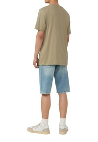 Olijfgroen t-shirt met korte mouwen, gecombineerd met lichtblauwe denim shorts. Casual sneakers met crèmekleurige accenten en witte enkelsokken.