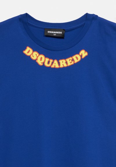 Μπλε μπλούζα με στρογγυλή λαιμόκοψη με τη λέξη "DSQUARED2" σε κίτρινο και πορτοκαλί κυρτό κείμενο κάτω από τη λαιμόκοψη και μια μαύρη ετικέτα μεγέθους μέσα στο γιακά.