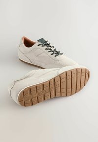 Sneaker in suede color beige chiaro con lacci scuri a contrasto. La suola in gomma presenta un motivo di grip dettagliato. Rivestimento interno morbido in marrone.