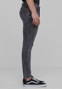 Fakó fekete farmer skinny nadrág közepes derékállással, cipzáras fly-vel és öt zsebel, fekete-fehér sportcipőkkel párosítva.