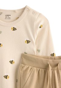 Jasno beżowy bawełniany zestaw składający się z bluzy z długim rękawem z printem pszczoły i zielonymi akcentami, w połączeniu z beżowymi spodniami z prążkowanym pasem.