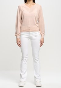 Hellrosa V-Ausschnitt-Pullover mit langen, leicht puffigen Ärmeln, kombiniert mit weißen, schmal geschnittenen Jeans und weißen strukturierten Sneakern.