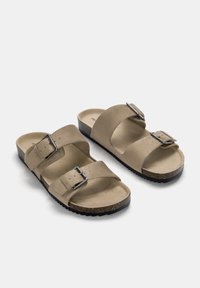 Beiga sandaler med två justerbara remmar och metallspännen. Mjuk material, formad fotbädd och en texturerad svart sula.