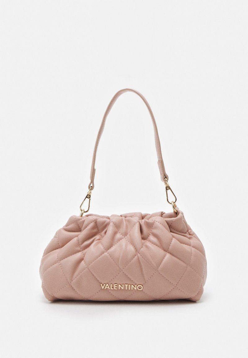 Quiltad rosa handväska med en texturerad yta, guldhardware och ett enda handtag. Har en samlad design med synlig sömnadsdetalj.