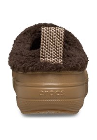 Crocs marrones con un upper de tela suave y texturizada y una correa tejida en el talón, que presenta una suela de goma lisa con la marca en el lateral.