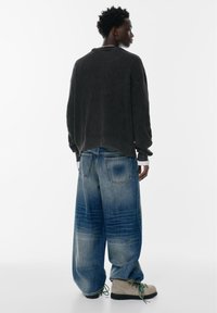 Texturerad svart ribbad långärmad tröja; löst sittande blåjeans med blekt tvätt och vida ben; ljusfärgade snörskor.