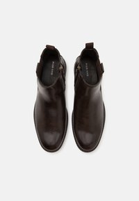 Botas de cuero marrón hasta el tobillo con un acabado suave, cierre de cremallera en el costado y lengüeta en la parte posterior. Diseño de punta redondeada.