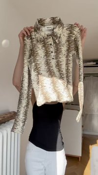 Garās piedurknes blouse ar krēmgaišiem un brūniem abstraktiem rakstiem, ar apkakli, pogu aizdari un mīkstu, teksturētu audumu.