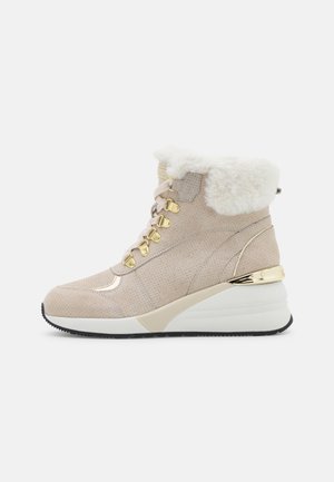 Sneaker alto beige con tomaia in suede texturizzato, colletto in pelliccia sintetica, dettagli in metallo dorato e tacco a zeppa per un'ulteriore elevazione.