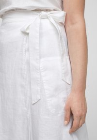 Witte linnen rok met een strik taille, zijzak en een zachte textuur. De stof valt soepel, wat de natuurlijke uitstraling versterkt.