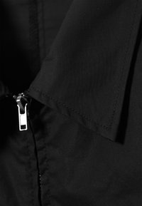 Gros plan d'une veste en tissu noir avec une fermeture éclair argentée et un col superposé.