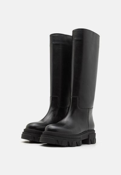 Črne zadrge do kolen, narejene iz gladke usnja, z masivnim teksturiranim podplatom in minimalnim šivom za eleganten dizajn.