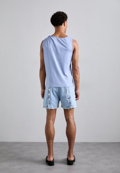 Light blue sleeveless top paired with denim shorts featuring gold buttons on the side and frayed edges. Black platform shoes.