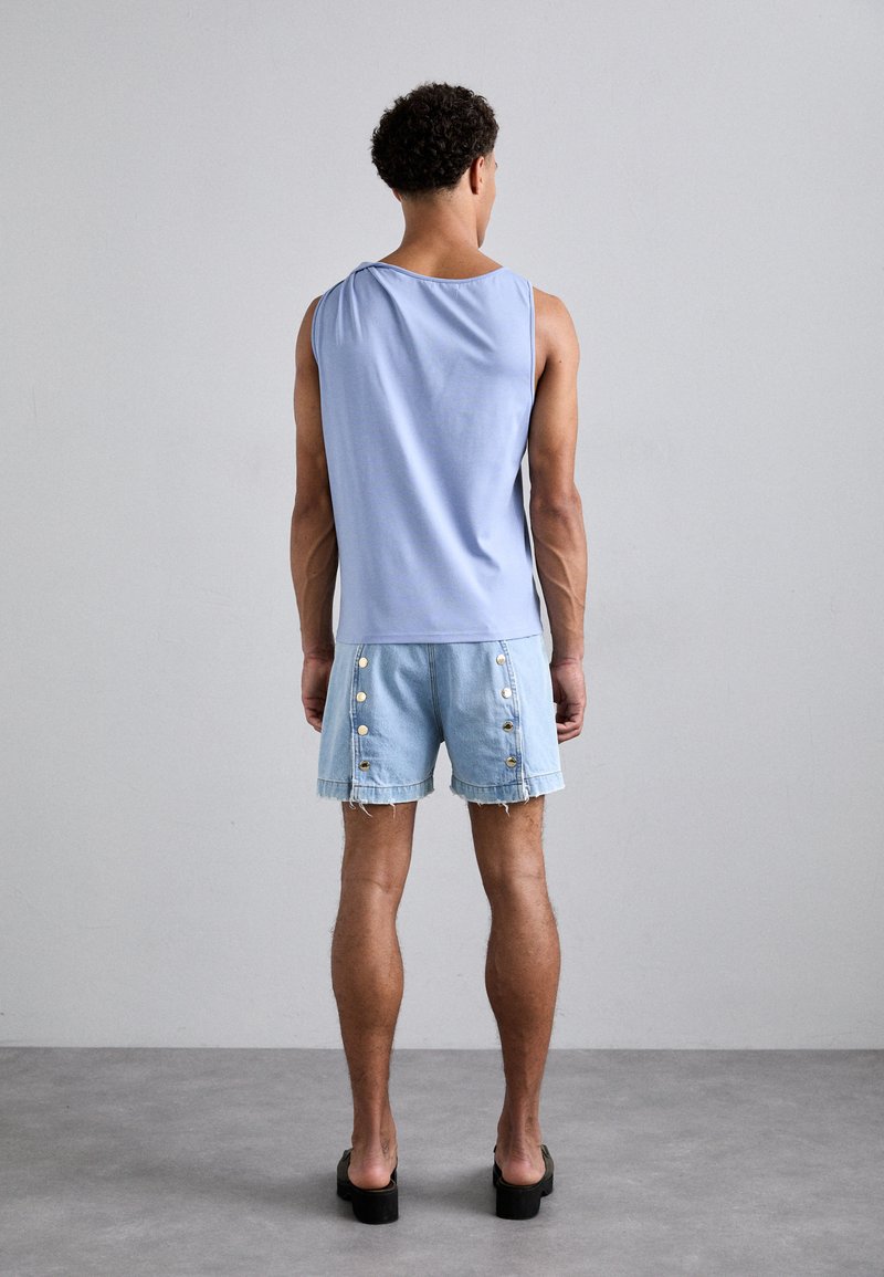 Lichtblauwe mouwloze top gecombineerd met denim shorts met gouden knopen aan de zijkant en rafelige randen. Zwarte platform schoenen.