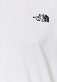 Vit bomullströja med en svart "The North Face"-logotyp på vänster bröstområde. Mjuk tyg med en slät yta.