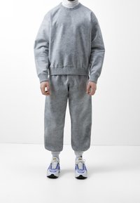 Gray textured sweatshirt with matching wide-legged trousers. Outfit features a high neckline and white sneakers with blue accents.