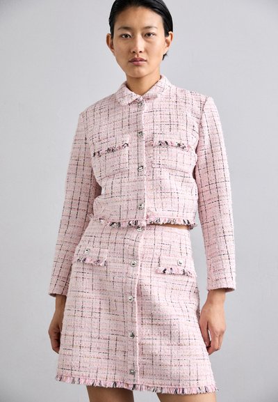 Rosa tweed co-ord sett med kragejakke som har klafflommer og knappelukking, og et matchende skjørt med frynse-detaljer.