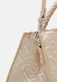 Sac à main beige avec une finition texturée, un motif de logo embossé, une poignée tressée et des accents en métal argenté pour la fermeture.