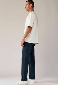 T-shirt met korte mouwen in crème kleur, gecombineerd met marineblauwe broek en witte sneakers. De stof lijkt glad, met een losse pasvorm en een eenvoudig ontwerp.