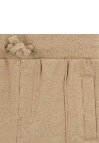 Los joggers de punto color beige tienen una cintura con cordón y un detalle de nudo, dos bolsillos laterales y una tela texturizada con sutiles variaciones.
