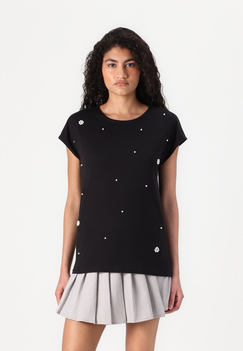 Black short-sleeve top with scattered faux pearl embellishments; paired with a light gray pleated skirt; smooth fabric and relaxed fit.