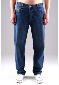 Dunkelblaue Jeans im geraden Schnitt, fünf Taschen, Kupfernieten und tonales Nähen. Kombiniert mit weißen Sneakern.