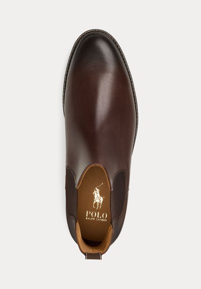 Bota de cano curto em couro castanho com painéis laterais elásticos, biqueira arredondada e detalhes costurados. O interior apresenta um forro bege e logótipo.