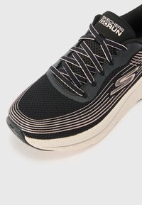 Chaussure de sport en mesh noir avec un design lisse et texturé. Elle présente des lignes d'accentuation blanches, des détails gris et une semelle épaisse et rembourrée.