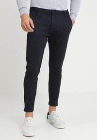 Marinblå randiga byxor i skräddarsydd passform, med dragkedja och uppvikta fållar, kombinerat med vita sneakers för en avslappnad look.