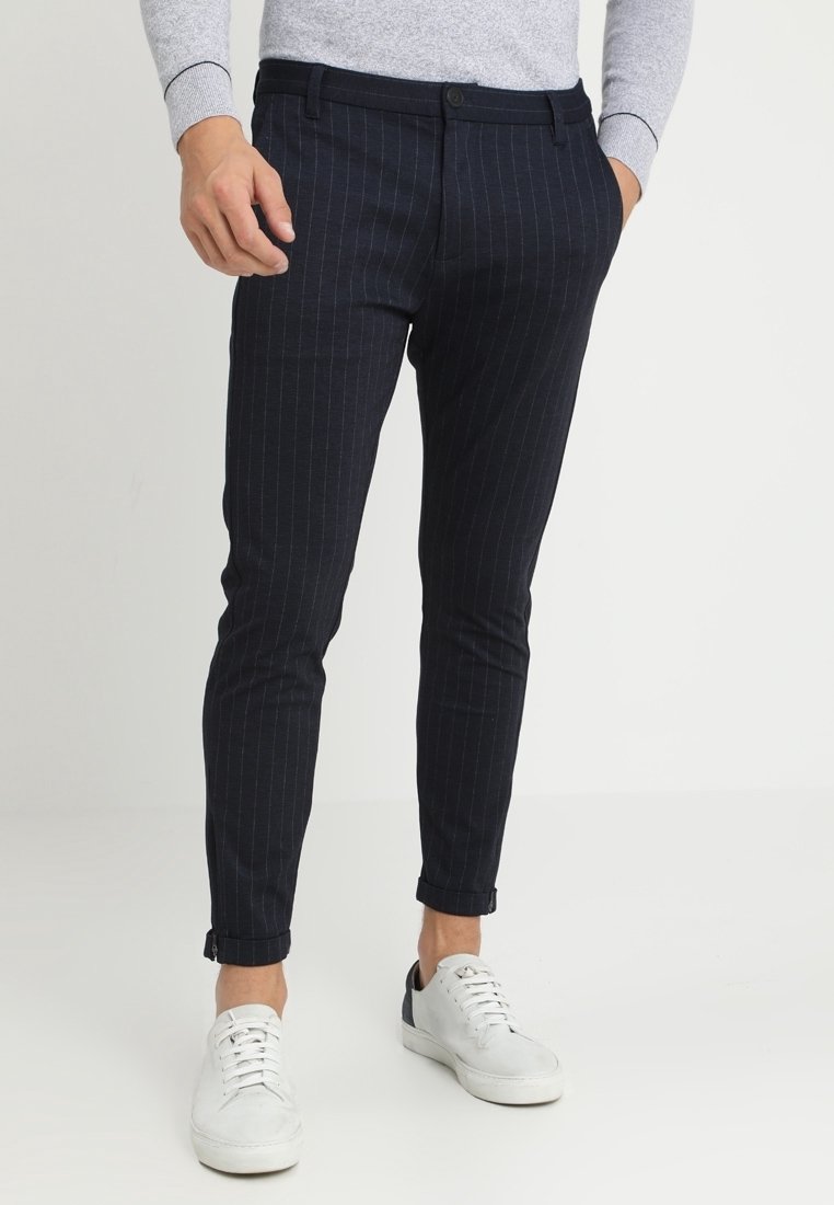 Marinblå randiga byxor i skräddarsydd passform, med dragkedja och uppvikta fållar, kombinerat med vita sneakers för en avslappnad look.