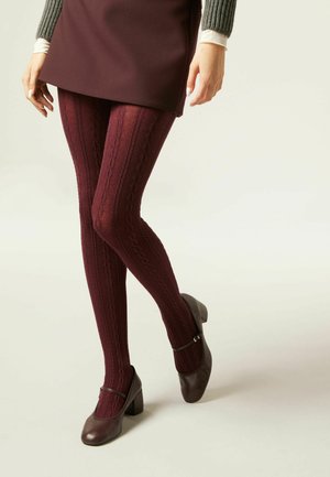 Collants tricotés bordeaux à motif de torsades, associés à des escarpins Mary Jane marron foncé, le tout porté avec une robe courte.