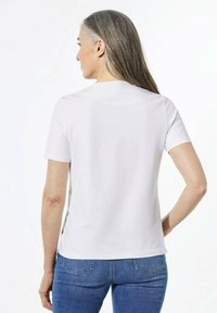 Weißes T-Shirt mit kurzen Ärmeln und runder Ausschnitt, glatte Textur und leicht taillierte Passform. Kombiniert mit blauen Jeans.