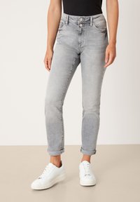 Jeans in denim grigio con design aderente, vita alta, due bottoni frontali e risvolti, abbinati a sneakers bianche con lacci.